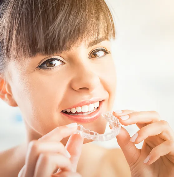 Smiling woman holding a clear aligner.
