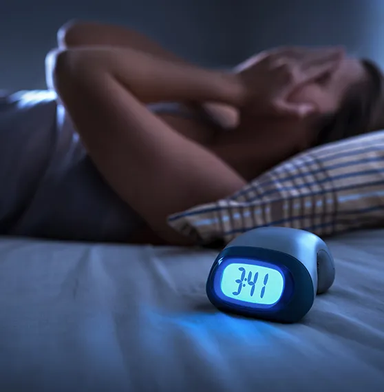 Person lying awake in bed at night with hands covering their face, illuminated by a clock showing 3:41 AM.