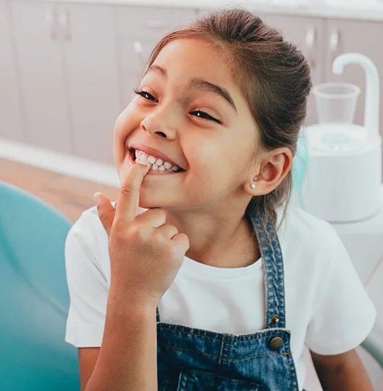 Happy young girl in a dental chair pointing to her tooth with a bright smile.
