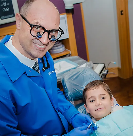 Dr. Boris in blue scrubs smiling beside a young boy seated in a dental chair.
