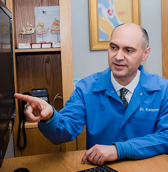 Dentist, Dr.Boris, in a blue coat pointing at a screen during a consultation in a well-organized office.