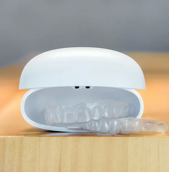 Clear dental aligners in a white storage case placed on a wooden surface.