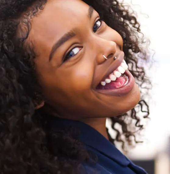 Smiling woman with curly hair and a nose ring, radiating joy and confidence.